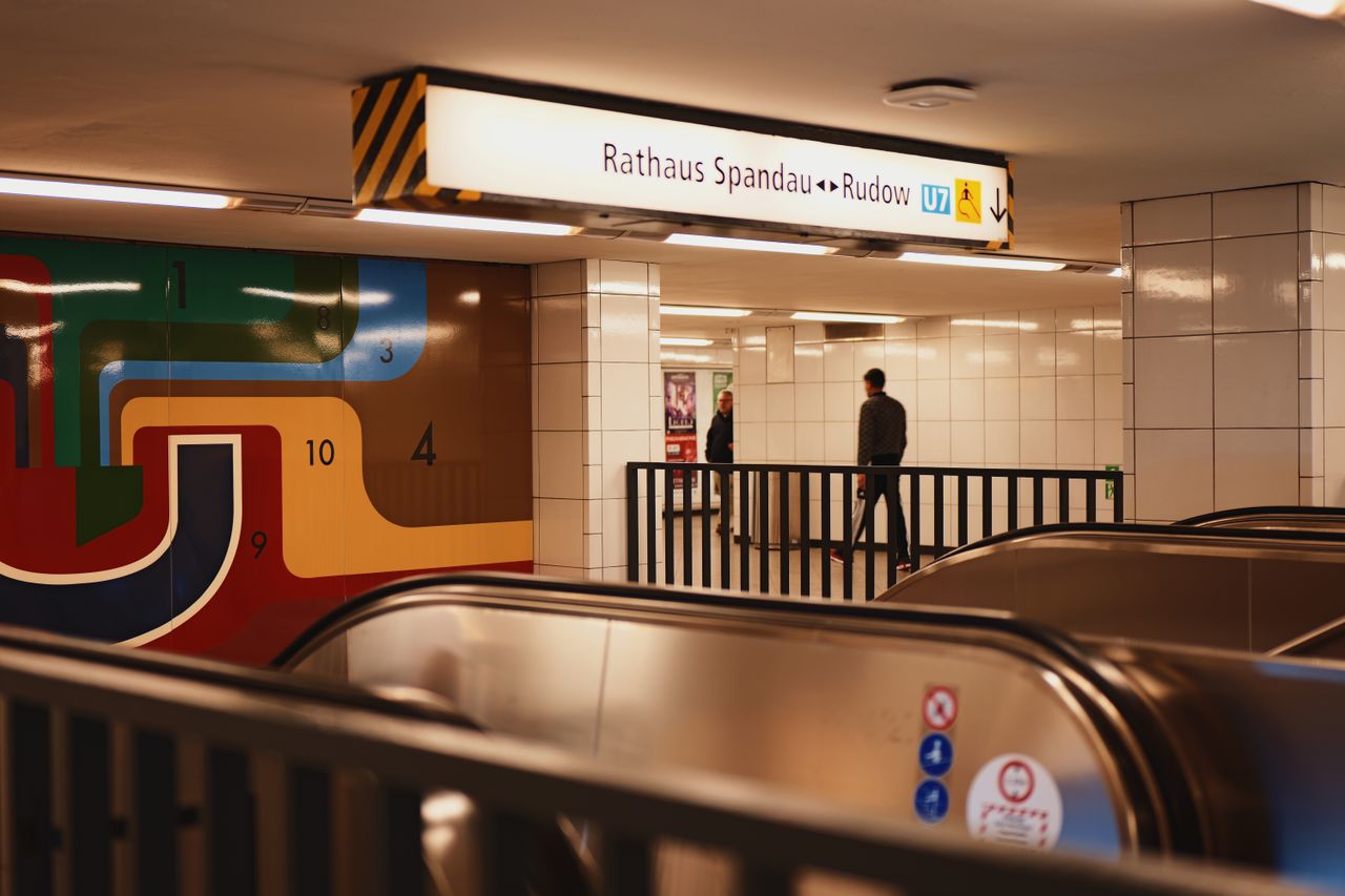 Vibrant Berlin subway station scene featuring passengers on an escalator with striking wall art.
